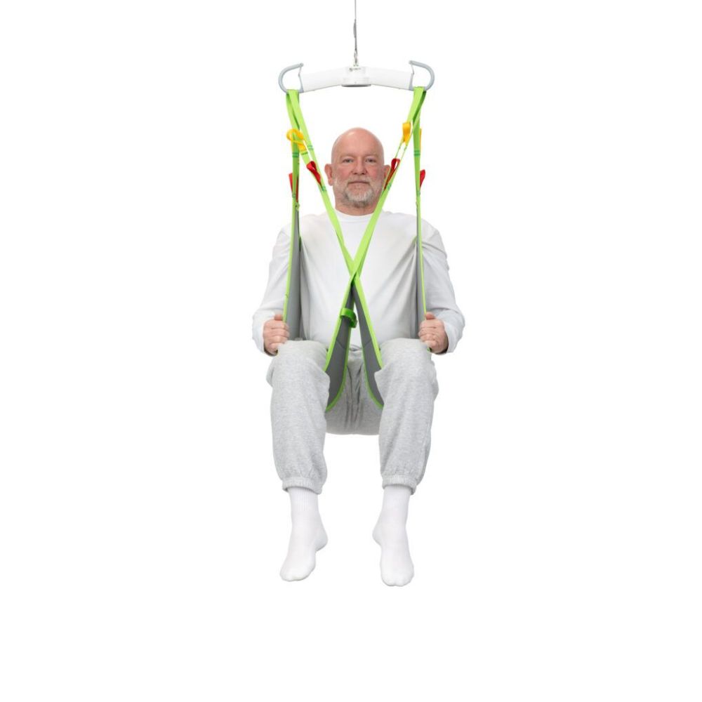 An older man in white clothing sits in a green Human Care Low Basic Sling, suspended in midair against a plain white background.