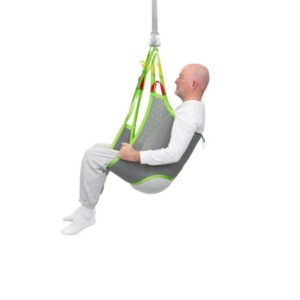 A bald man in white clothing sits in a gray and green Human Care Low Basic Sling, suspended and supported by straps, against a plain white background.