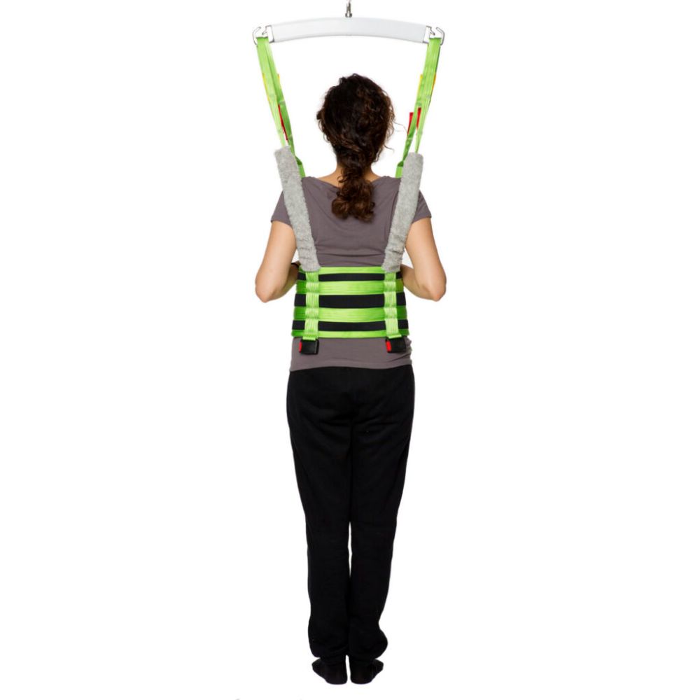 A person wearing a green safety harness, identified as the Human Care Multi Sling, is suspended from overhead supports and shown from the back against a plain white background.