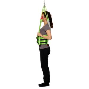 Person standing upright wearing a green Human Care Multi Sling patient lift harness attached to an overhead support, demonstrating a medical lifting aid.