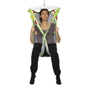 A woman sits upright in a green and gray Human Care Silhouette Sling, holding the straps with both hands.