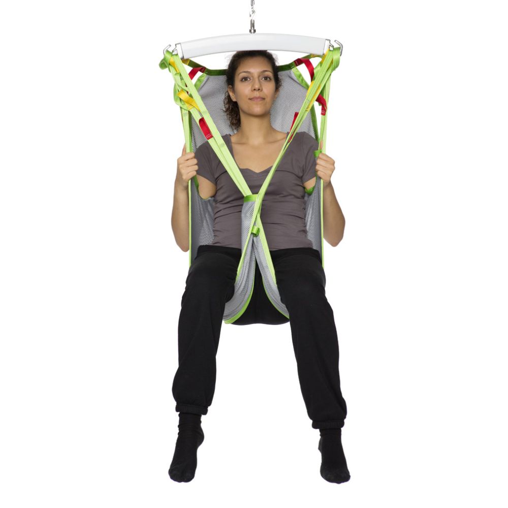 A woman sits upright in a green and gray Human Care Silhouette Sling, holding the straps with both hands.