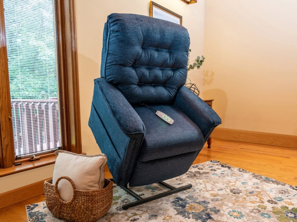 A blue recliner chair in an upright, lifted position in a living room, with a control remote on the seat and a woven basket containing pillows beside it.