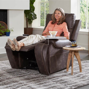A woman lounges with her feet up in the Titan Lift Chair, enjoying a bowl of popcorn. A drink rests on a small wooden side table next to her.