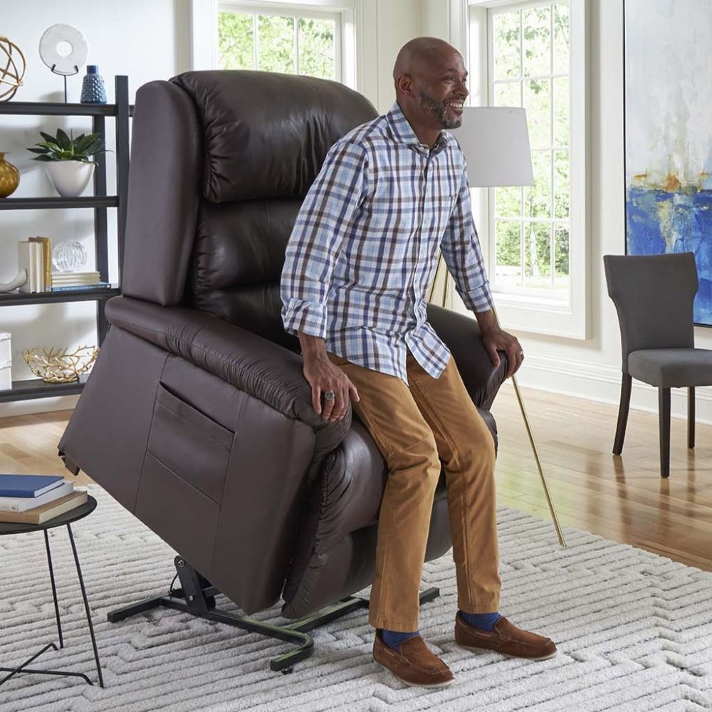 A man uses a brown reclining lift chair to assist him in standing up in a bright, modern living room.