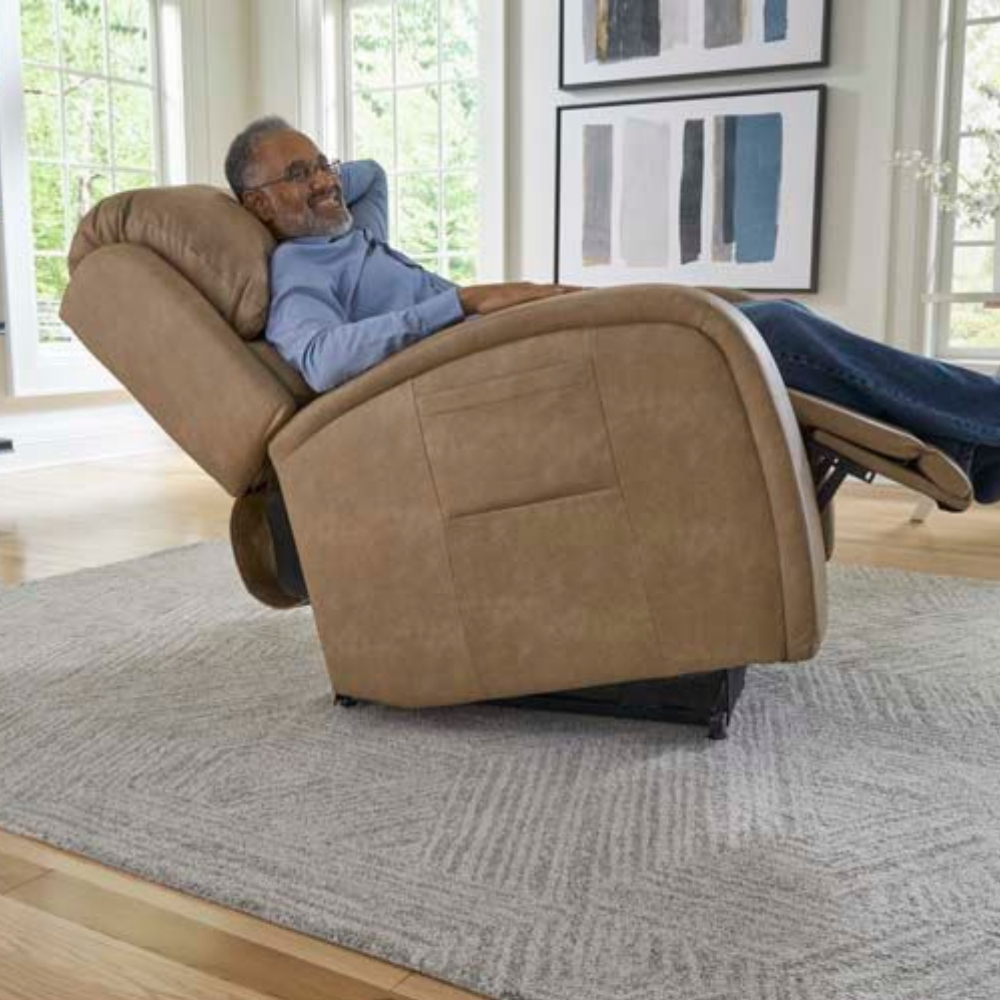 A man reclines in an EZ Sleeper with Twilight Lift Chair, tan color, on a gray rug in a bright living room with abstract art on the wall.