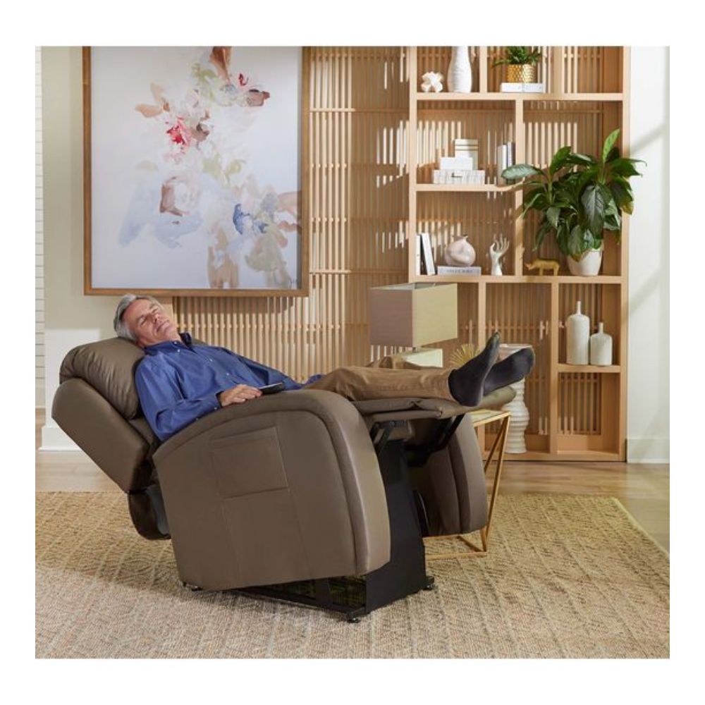 An older man reclines with his eyes closed in an EZ Sleeper Slim armchair, set in a modern living room decorated with shelves, plants, and stylish decor.