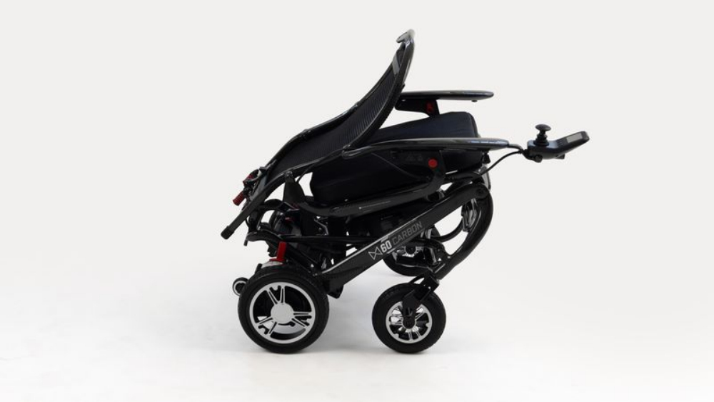 Side view of a Monarch Mobility MM60 Carbon folding power wheelchair featuring a joystick controller and a carbon fiber-patterned frame.