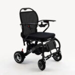 A black, foldable Monarch Mobility MM60 Carbon electric wheelchair with a mesh backrest and joystick controller on the armrest.