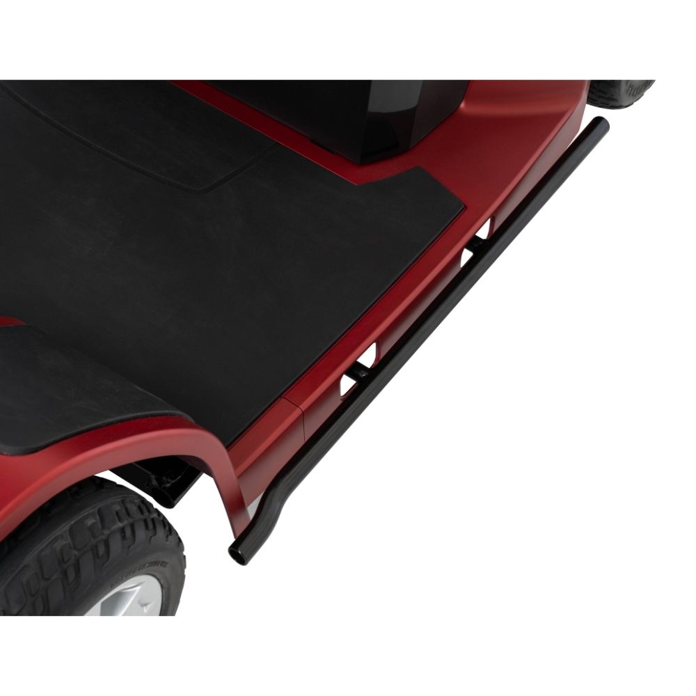 Close-up of a red Maxima 4-Wheel Scooter’s black side step and tire, highlighting the textured floor mat and part of the wheel well.