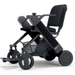 WHILL Model F folding, lightweight electric wheelchair with a black frame, mesh seat, armrests, footrest, and large rear wheels, shown on a white background.