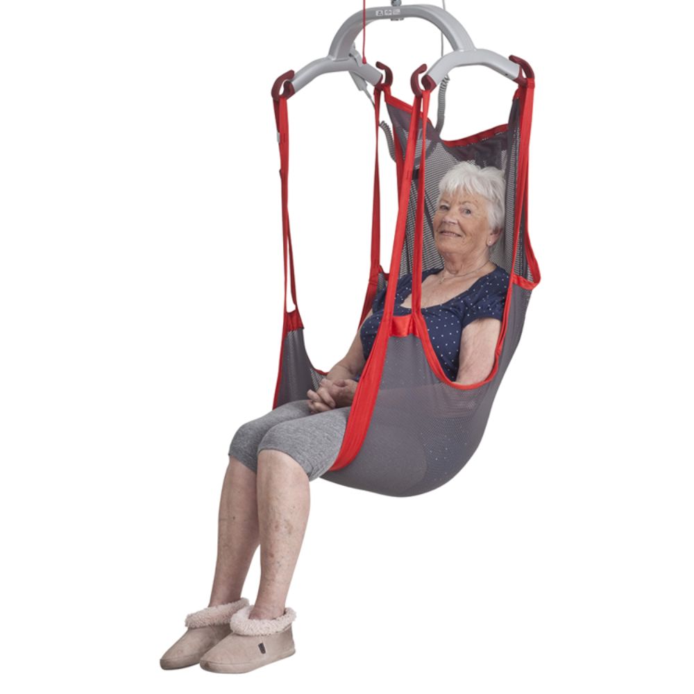 An elderly woman sits in a Molift RgoSling Comfort Highback Net gray and red mesh sling lift, wearing slippers and casual clothes, with her hands resting on her lap.