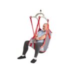 An older man is seated in a Molift RgoSling Mediumback Padded lift sling, secured by straps and suspended from a mechanical lift, with a white background.