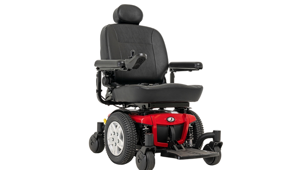 A Jazzy 600ES Power Wheelchair in red and black, featuring a padded seat, headrest, armrests, joystick control, and footrest, is displayed against a plain white background.