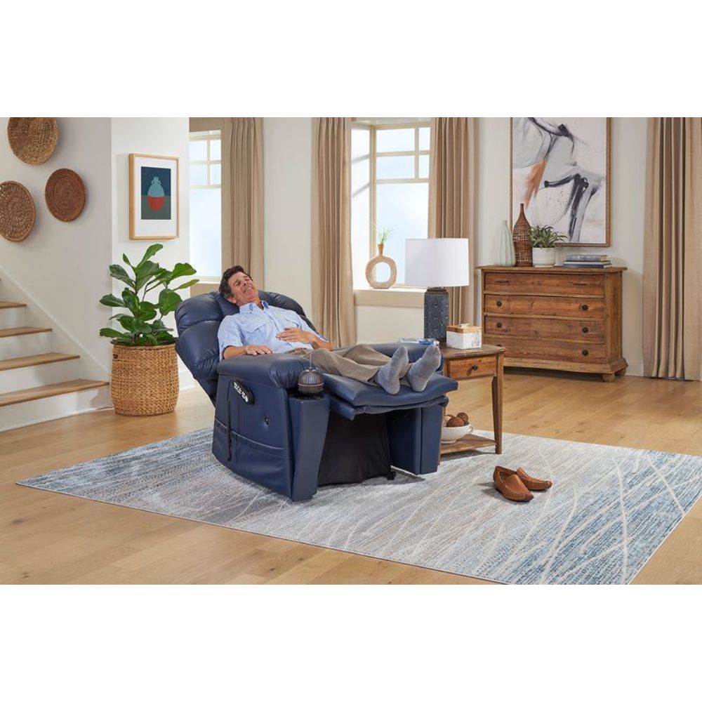 A man reclines with his feet elevated in the Cloud Supreme with Twilight Lift Chair, set in a bright living room featuring wooden furniture, a rug, and decorative items.