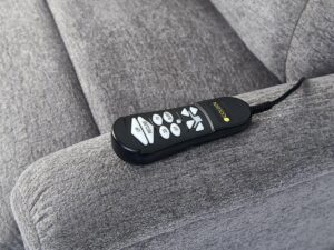 A Comforter with MaxiComfort Lift Chair features a black COOSWAY remote with white buttons resting on its gray upholstered arm.