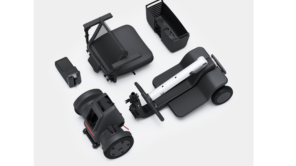 A modular robot, inspired by the WHILL Model R 3-Wheel, is taken apart into components—such as the wheels, battery, main body, basket, and connecting bars—and displayed neatly on a white surface.