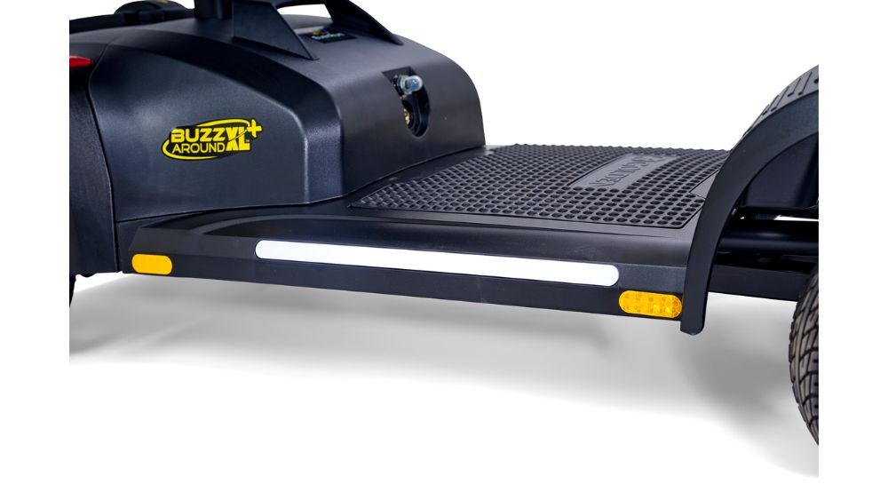 Close-up of a black platform with the Buzzaround logo, featuring a textured footrest and reflective side strips—designed specifically for the Buzzaround XL+ 4-Wheel Scooter.