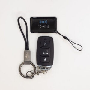A black Monarch Mobility Smarti Plus key fob with three function icons, a matching keychain with a cord loop, and a rectangular NFC tag.