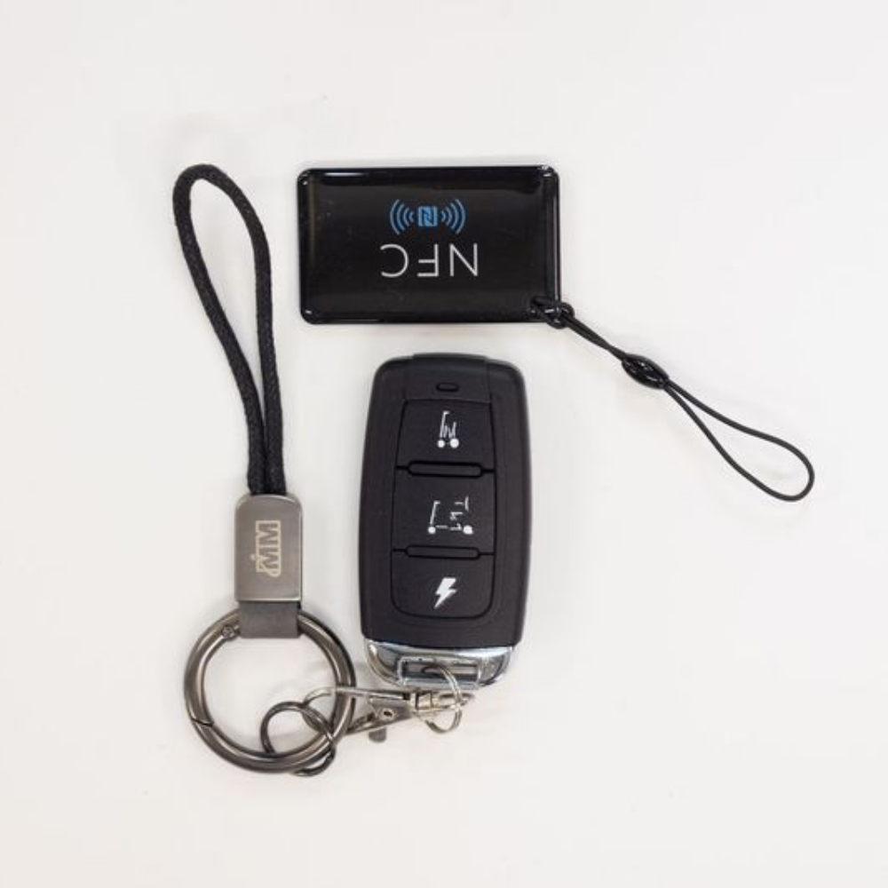 A black Monarch Mobility Smarti Plus key fob with three function icons, a matching keychain with a cord loop, and a rectangular NFC tag.