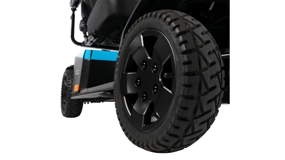 Close-up view of black, rugged tires on a lawnmower, reminiscent of the sturdy wheels found on the PX4 4-Wheel Scooter, with part of the blue and black mower body visible in the background.