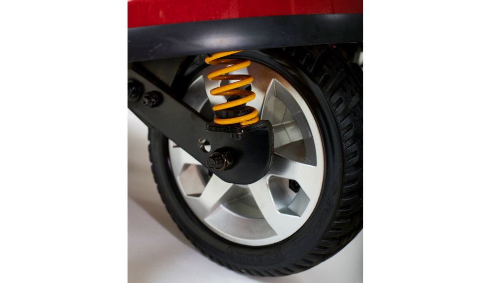 Close-up of the black rubber wheel with a silver rim and yellow coil spring suspension on the Companion Full-Size 3-Wheel Scooter in red.