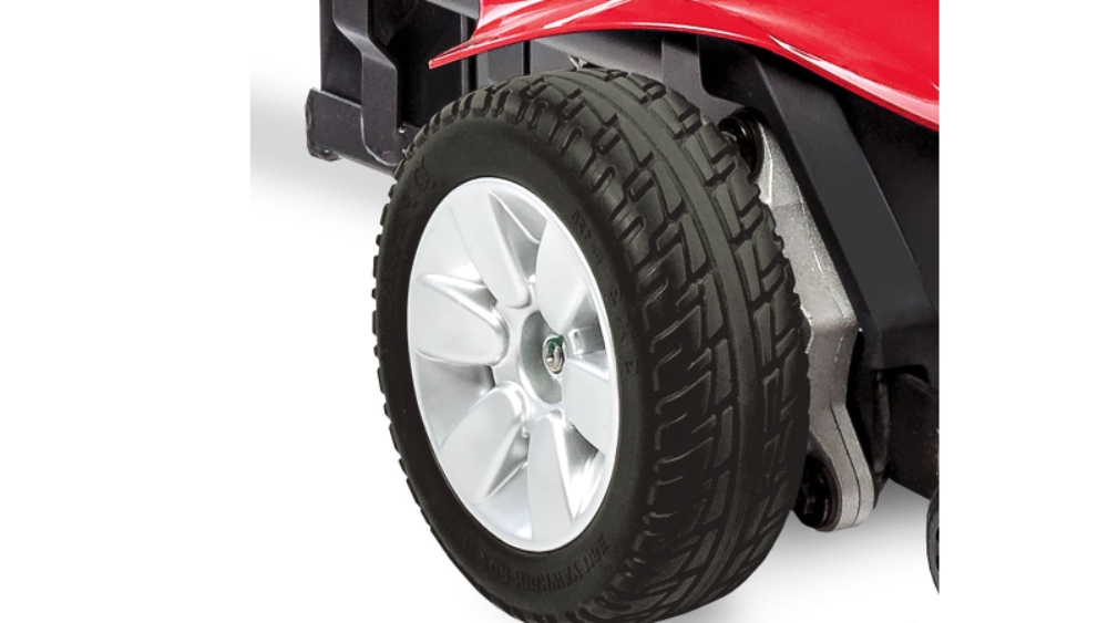 Close-up of a black, treaded wheel with a silver rim attached to a red Jazzy Elite ES Power Wheelchair.