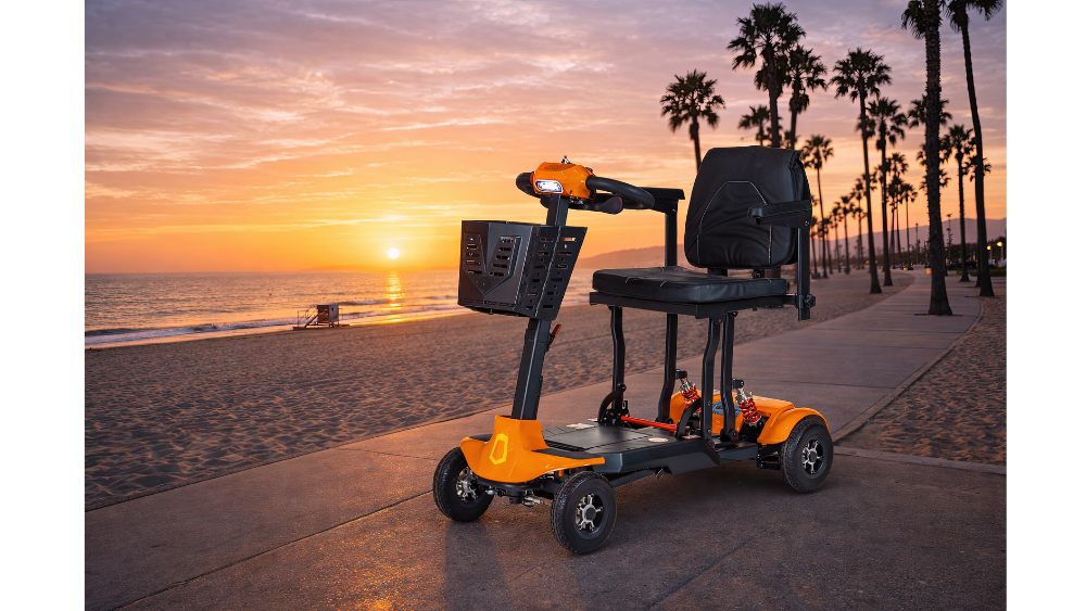 An orange and black Monarch Mobility Genie Auto parked on a beach boardwalk at sunset.