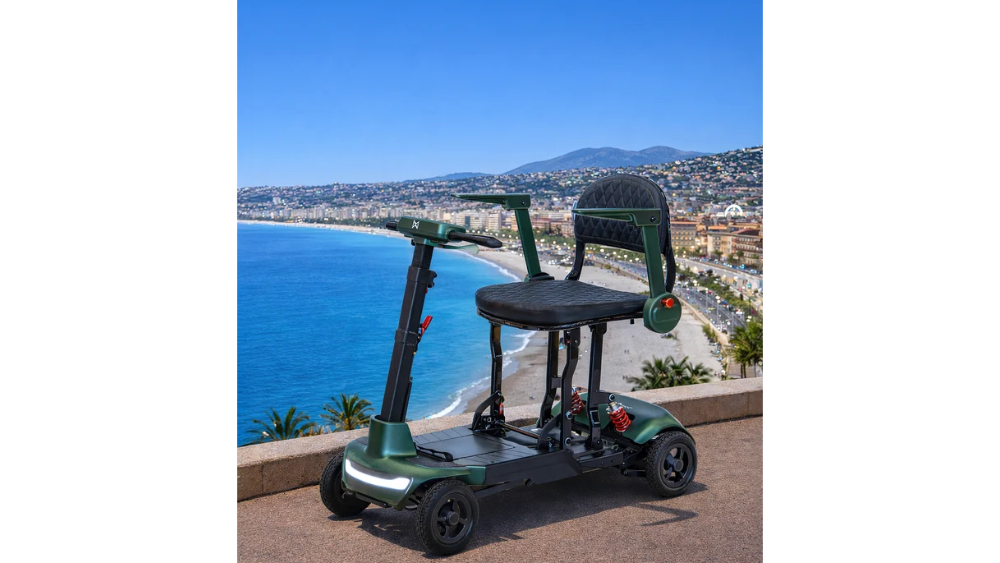 A dark green Monarch Mobility Smarti Plus four-wheeled mobility scooter with a black padded seat and armrests, parked on a seaside promenade overlooking a beach and bay.
