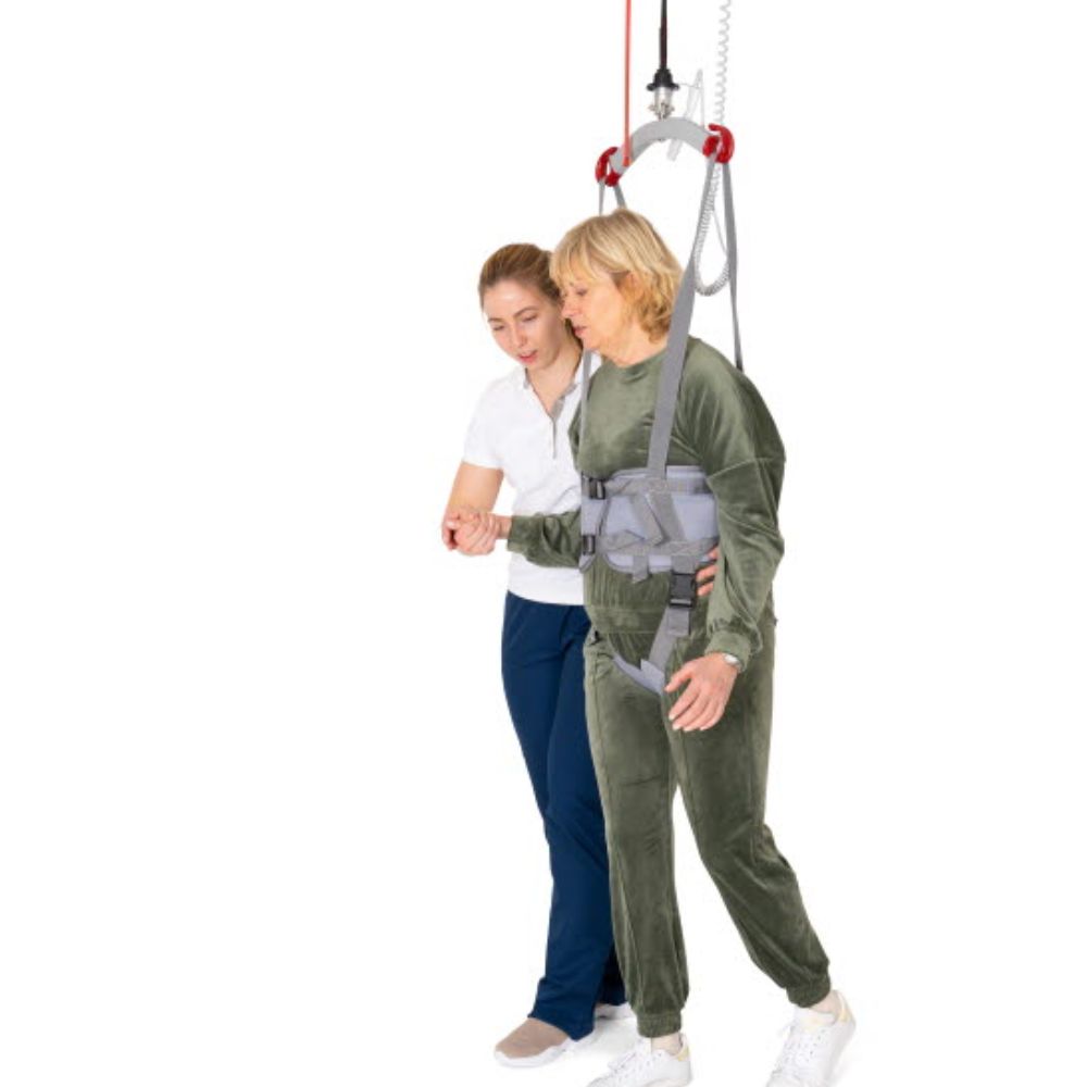 A therapist supports a woman walking with the UnoSling Ambulation Vest, suspended from the ceiling—an effective aid for rehabilitation and physical therapy.