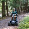 A person rides the Baja™ Wrangler® 2 4-Wheel Scooter along a forest path, surrounded by trees and ferns.