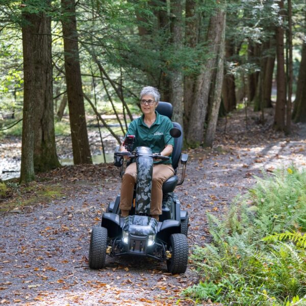 A person rides the Baja™ Wrangler® 2 4-Wheel Scooter along a forest path, surrounded by trees and ferns.