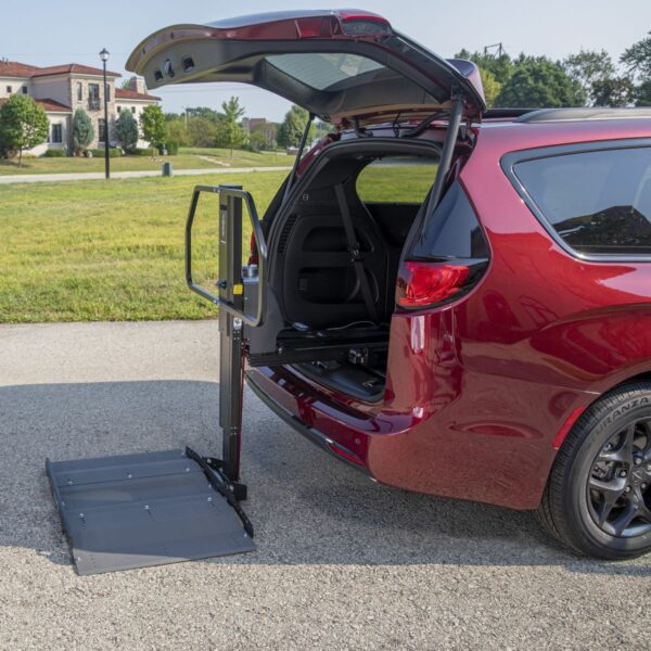 A red minivan with its rear hatch open displays a deployed Bruno Joey Platform Style Interior Lift (VSL-4400) wheelchair system on a paved driveway.