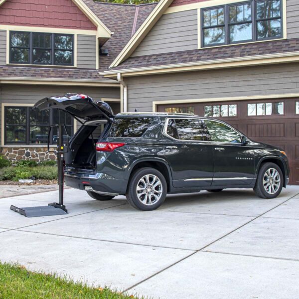 A black SUV is parked in a driveway with its rear hatch open, showcasing a Bruno Joey Platform Style Interior Lift (VSL-4400) at the back for convenient loading and unloading.