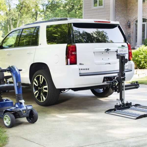 A white SUV with a Bruno Out-Sider® (ASL-275) scooter lift is parked in a driveway beside a blue mobility scooter.