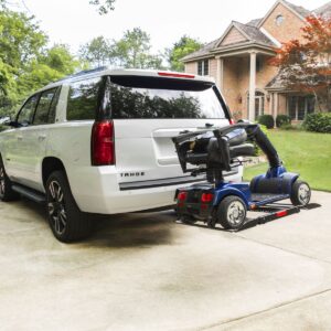 A Bruno Out-Sider® (ASL-275) scooter lift is mounted to the rear of a white Chevrolet Tahoe, carrying a mobility scooter on a platform in a residential driveway.