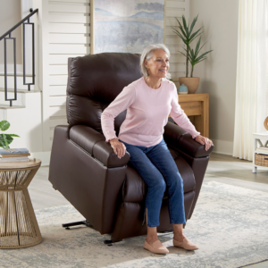 An older woman in a pink sweater stands up from the brown Cloud+ Lift Chair in a bright, modern living room.