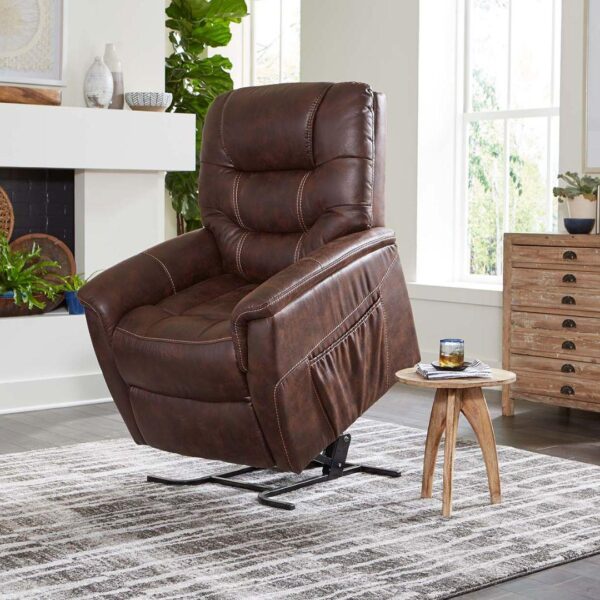 The Dione Lift Chair, a brown leather recliner, is partially lifted on a patterned rug beside a wooden side table with a drink in a bright living room.