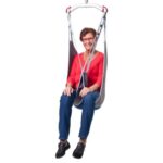 An adult wearing a red shirt and blue pants is comfortably seated in a Molift EvoSling MediumBack Net Padded, securely supported by a harness attached to its sturdy metal frame.