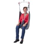 A person wearing a red top, jeans, and black shoes sits in a Molift EvoSling MediumBack Padded chair lift with a metal frame, against a white background.