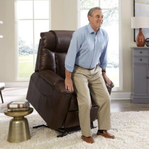 An older man stands up from a Rhea Lift Chair, a brown leather power lift recliner, in a bright living room with neutral decor.